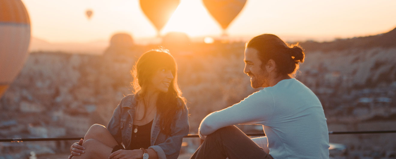 una ragazza e un ragazzo seduti al tramonto con mongolfiere come sfondo